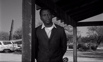 Movie still from “Lilies of the Field” (1963), directed by Ralph Nelson – A black and white photo of a man standing under a wooden structure; Medium shot, Low angle