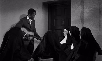 Movie still from “Lilies of the Field” (1963), directed by Ralph Nelson – A man and a nun playing a guitar and singing; Medium shot, High angle