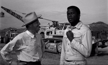 Movie still from “Lilies of the Field” (1963), directed by Ralph Nelson – Two men standing next to each other in front of construction equipment; Medium shot, Over the shoulder angle