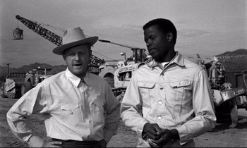 Movie still from “Lilies of the Field” (1963), directed by Ralph Nelson – Two men standing next to each other in front of a helicopter; Medium shot, Over the shoulder angle
