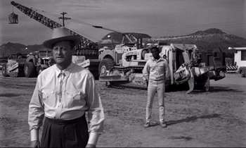 Movie still from “Lilies of the Field” (1963), directed by Ralph Nelson – Two men standing next to each other in front of some construction equipment; Medium shot, Over the shoulder angle