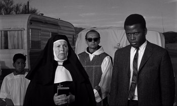 Movie still from “Lilies of the Field” (1963), directed by Ralph Nelson – A group of people standing next to each other in front of a trailer; Medium shot, Over the shoulder angle