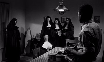 Movie still from “Lilies of the Field” (1963), directed by Ralph Nelson – A group of nuns standing around a table with a man sitting at the table; Wide shot, Low angle