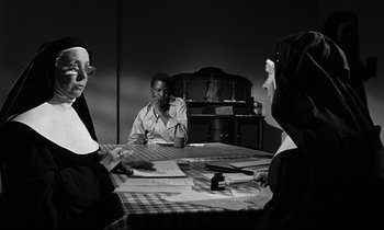 Movie still from “Lilies of the Field” (1963), directed by Ralph Nelson – A group of people sitting around a table; Medium shot, Over the shoulder angle