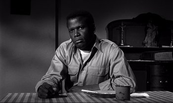 Movie still from “Lilies of the Field” (1963), directed by Ralph Nelson – A man sitting at a table with a cup of coffee in front of him; Medium shot, Low angle