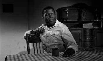 Movie still from “Lilies of the Field” (1963), directed by Ralph Nelson – A man sitting at a table with a cup in his hand; Medium shot, Over the shoulder angle