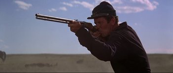 Movie still from “Little Big Man” (1970), directed by Arthur Penn – A man is aiming a rifle in a field; Close Up shot, Low angle