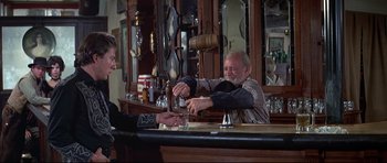 Movie still from “Little Big Man” (1970), directed by Arthur Penn – A man sitting at a bar with a glass of water; Medium shot, Low angle