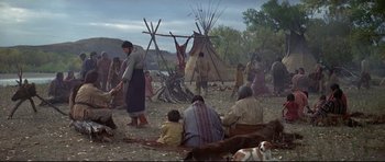 Movie still from “Little Big Man” (1970), directed by Arthur Penn – A group of people sitting and standing in front of a teepee; Wide shot, Low angle