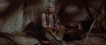 Movie still from “Little Big Man” (1970), directed by Arthur Penn – An older native american sitting on the ground; Medium shot, Low angle