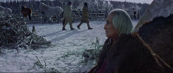 Movie still from “Little Big Man” (1970), directed by Arthur Penn – An older man sitting in the snow next to horses; Medium shot, Over the shoulder angle