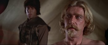 Movie still from “Little Big Man” (1970), directed by Arthur Penn – A man with long hair and a mustache is standing next to another man with long hair; Close Up shot, Over the shoulder angle