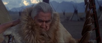 Movie still from “Little Big Man” (1970), directed by Arthur Penn – An old man with a gray beard is holding a fur coat over his face; Close Up shot, Low angle