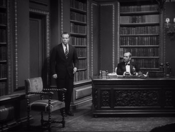Movie still from “Little Caesar” (1931), directed by Mervyn LeRoy – A man standing in front of a desk in front of a chair; Wide shot, High angle