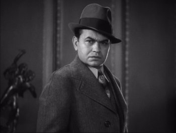 Movie still from “Little Caesar” (1931), directed by Mervyn LeRoy – A man wearing a suit and a hat in front of a wall; Close Up shot, Low angle