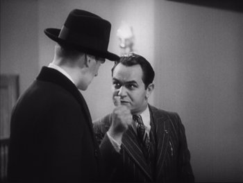 Movie still from “Little Caesar” (1931), directed by Mervyn LeRoy – A man in a suit and a man in a hat looking at himself in the mirror; Close Up shot, Over the shoulder angle