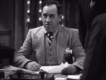 Movie still from “Little Caesar” (1931), directed by Mervyn LeRoy – An old photo of a man sitting at a table with papers; Medium shot, Low angle