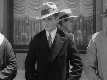 Movie still from “Little Caesar” (1931), directed by Mervyn LeRoy – Black and white photograph of a man wearing a suit and a hat; Medium shot, Low angle