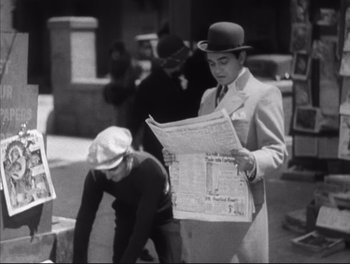 Movie still from “Little Caesar” (1931), directed by Mervyn LeRoy – A man wearing a hat and holding a newspaper while standing next to another man in a hat; Medium shot, Low angle