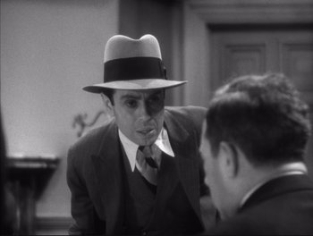 Movie still from “Little Caesar” (1931), directed by Mervyn LeRoy – A man wearing a suit and a hat talking to another man in a suit; Close Up shot, Over the shoulder angle