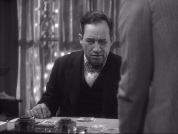 Movie still from “Little Caesar” (1931), directed by Mervyn LeRoy – A black and white photo of a man sitting at a table with cards; Medium shot, Over the shoulder angle