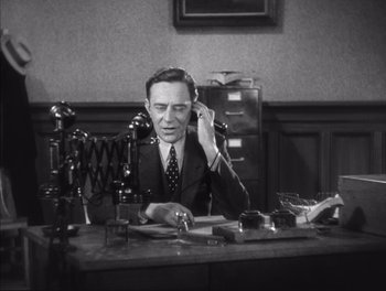 Movie still from “Little Caesar” (1931), directed by Mervyn LeRoy – A man sitting at a desk talking on a phone; Medium shot, High angle