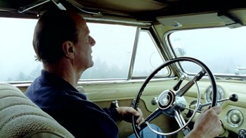 Movie still from “Little Dieter Needs to Fly” (1997), directed by Werner Herzog – A man sitting in the driver's seat of an old car; Medium shot, Low angle