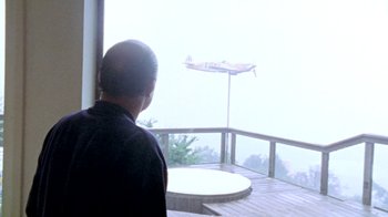Movie still from “Little Dieter Needs to Fly” (1997), directed by Werner Herzog – A man standing on a deck looking out a window; Extreme Wide shot, Low angle
