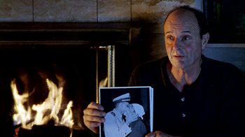 Movie still from “Little Dieter Needs to Fly” (1997), directed by Werner Herzog – A man holding up a picture of a man in uniform; Close Up shot, Over the shoulder angle