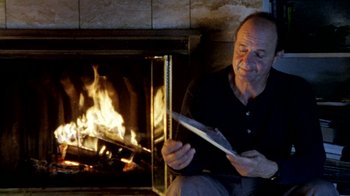 Movie still from “Little Dieter Needs to Fly” (1997), directed by Werner Herzog – A man sitting in front of a fireplace holding a knife; Medium shot, Low angle