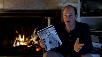 Movie still from “Little Dieter Needs to Fly” (1997), directed by Werner Herzog – A man holding an old photo in front of a fireplace; Close Up shot, Over the shoulder angle