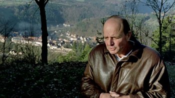 Movie still from “Little Dieter Needs to Fly” (1997), directed by Werner Herzog – A bald man in a brown leather jacket looks at the camera; Medium shot, High angle