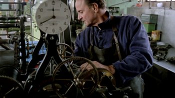 Movie still from “Little Dieter Needs to Fly” (1997), directed by Werner Herzog – A man working on a clock in a workshop; Medium shot, Low angle