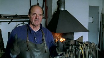 Movie still from “Little Dieter Needs to Fly” (1997), directed by Werner Herzog – A man in a blue shirt and apron standing in front of an open fire; Close Up shot, Low angle