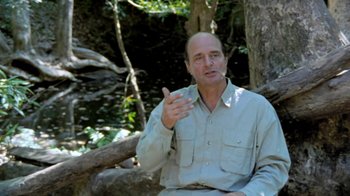 Movie still from “Little Dieter Needs to Fly” (1997), directed by Werner Herzog – A man in a white shirt is sitting in the woods; Medium shot, Over the shoulder angle