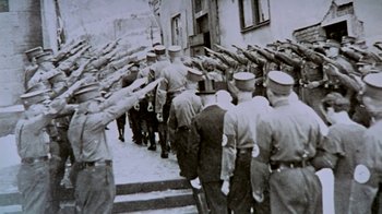 Movie still from “Little Dieter Needs to Fly” (1997), directed by Werner Herzog – A black and white photo of a group of men in uniform saluting; Wide shot, High angle