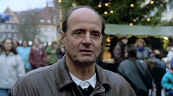 Movie still from “Little Dieter Needs to Fly” (1997), directed by Werner Herzog – An older man in a brown jacket is standing in front of a group of people; Close Up shot, Low angle