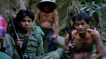 Movie still from “Little Dieter Needs to Fly” (1997), directed by Werner Herzog – A group of men sitting next to each other holding guns; Medium shot, High angle