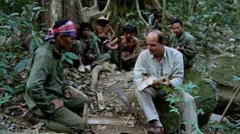 Movie still from “Little Dieter Needs to Fly” (1997), directed by Werner Herzog – A group of men sitting on the ground in the woods; Medium shot, High angle