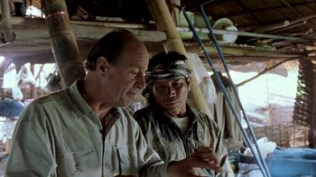 Movie still from “Little Dieter Needs to Fly” (1997), directed by Werner Herzog – A man and a man standing next to each other in front of a building; Medium shot, Over the shoulder angle