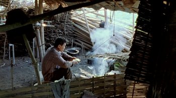 Movie still from “Little Dieter Needs to Fly” (1997), directed by Werner Herzog – A man is cooking food in an outdoor kitchen; Wide shot, High angle