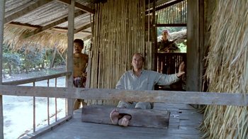 Movie still from “Little Dieter Needs to Fly” (1997), directed by Werner Herzog – A man sitting on the ground in front of two other men; Wide shot, High angle
