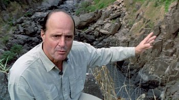 Movie still from “Little Dieter Needs to Fly” (1997), directed by Werner Herzog – A man in a gray shirt is standing by a river; Close Up shot, Low angle