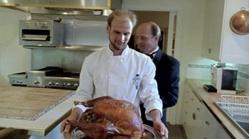 Movie still from “Little Dieter Needs to Fly” (1997), directed by Werner Herzog – A man holding a large turkey in a kitchen; Medium shot, Low angle