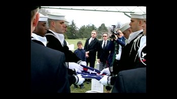 Movie still from “Little Dieter Needs to Fly” (1997), directed by Werner Herzog – A group of men holding a flag in front of a grave; Wide shot, Over the shoulder angle