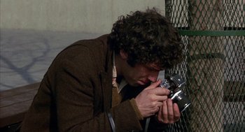 Movie still from “Little Murders” (1971), directed by Alan Arkin – A man taking a picture with a camera; Close Up shot, High angle
