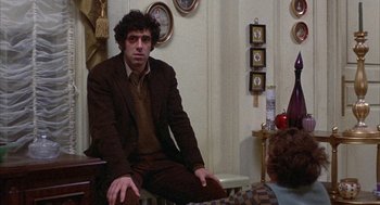 Movie still from “Little Murders” (1971), directed by Alan Arkin – A man sitting on a chair in front of a clock; Medium shot, Over the shoulder angle