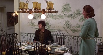 Movie still from “Little Murders” (1971), directed by Alan Arkin – A man sitting at a dinner table in front of a painting; Wide shot, High angle