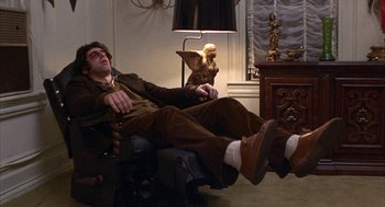 Movie still from “Little Murders” (1971), directed by Alan Arkin – A man sitting in a chair with his feet on the floor; Wide shot, High angle