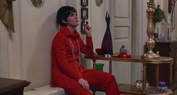 Movie still from “Little Murders” (1971), directed by Alan Arkin – A woman sitting on top of a bench in a room; Medium shot, Low angle